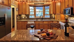 A kitchen with granite countertops, wooden cabinets, a stainless steel refrigerator, a microwave, and a wine bottle.