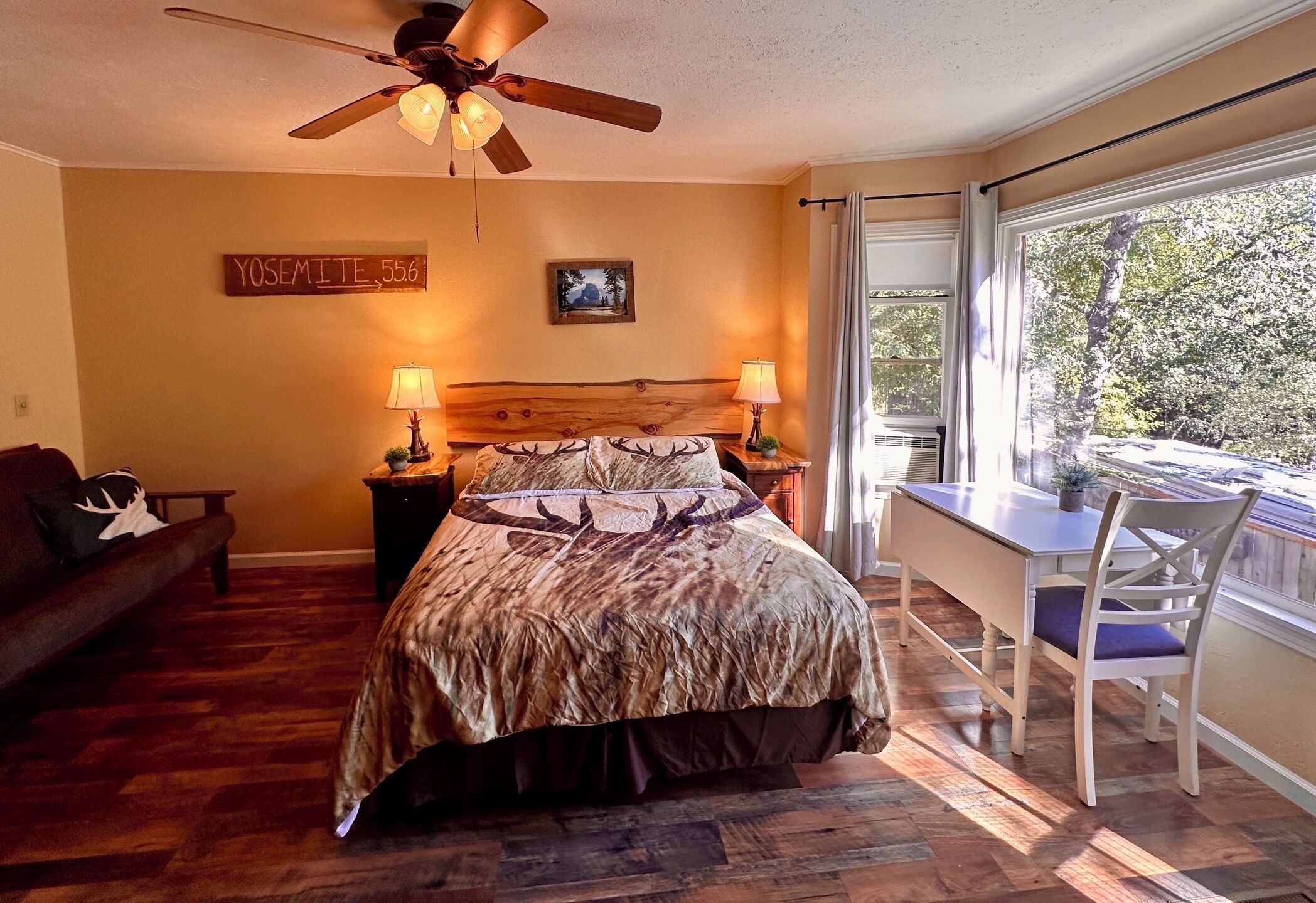 A bedroom with a bed, a desk, and a chair. There is a ceiling fan, a window, and a sign on the wall.