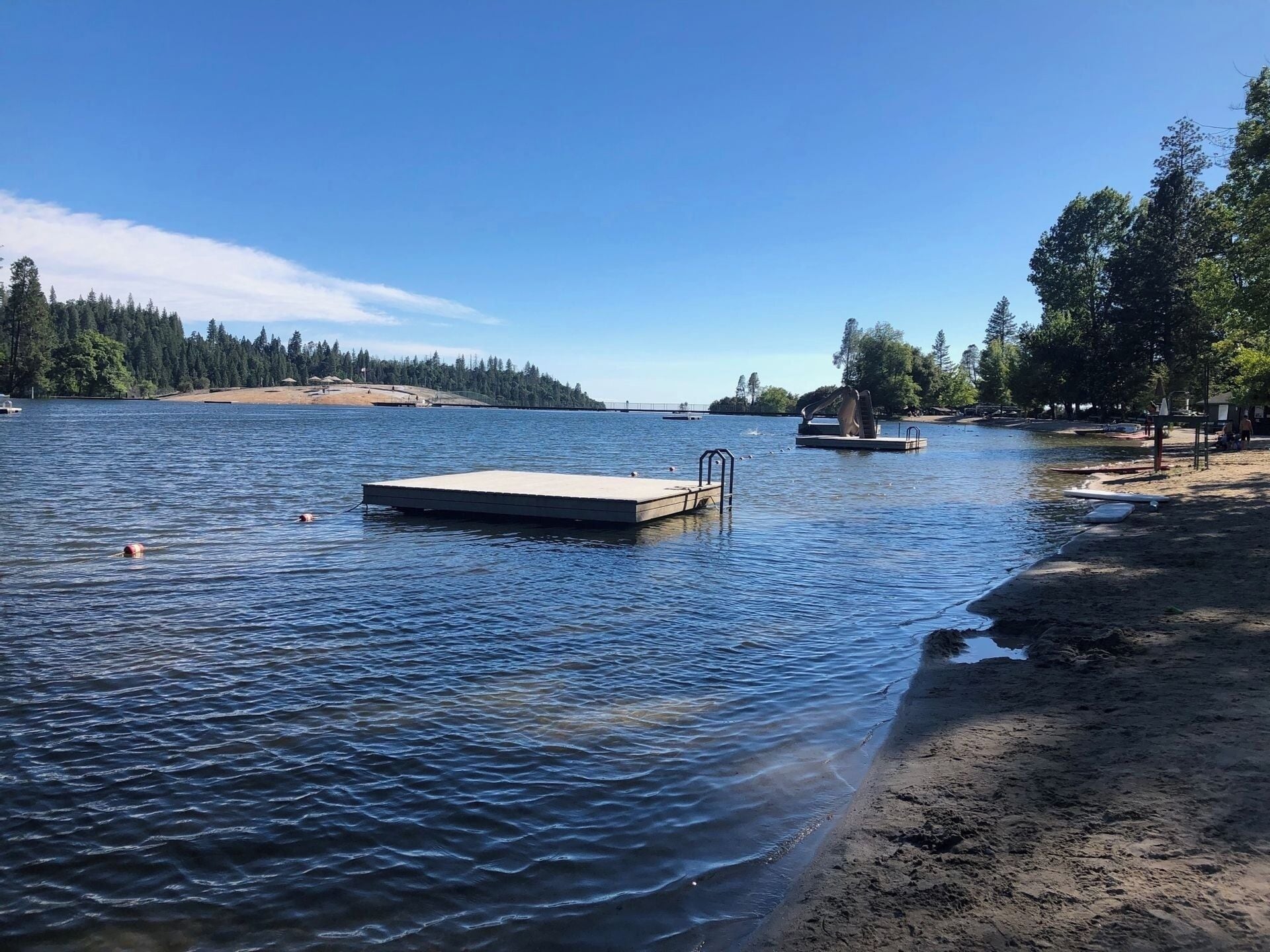 Un lago con un muelle de madera y una playa arenosa.