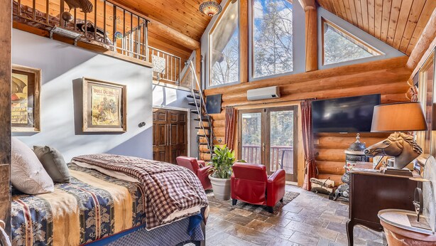 Interior acogedor de una cabaña de troncos con una cama grande, sillones rojos, una chimenea y un televisor.