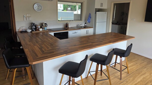 A modern kitchen with a wooden island, bar stools, a sink, and a refrigerator. - Middleton Halleedays - Beach getaway (Middleton)