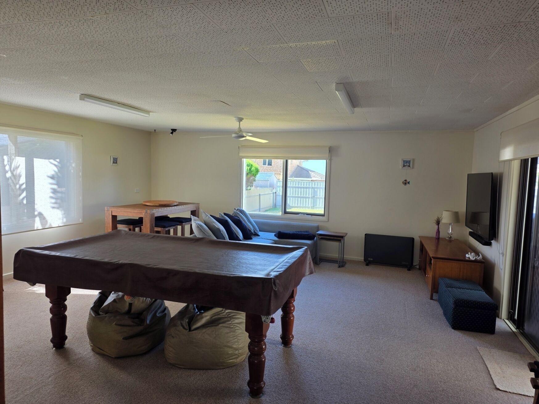 A room with a pool table, bean bag chairs, a small table with a lamp, and a TV.