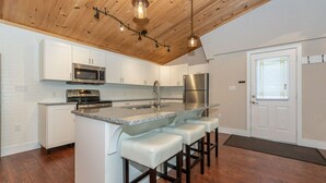 Una cocina moderna con armarios blancos, electrodomésticos de acero inoxidable, encimera de granito y techo de madera.