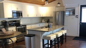 Una cocina moderna con techo de madera, electrodomésticos de acero inoxidable, una isla central con taburetes de bar y una zona de comedor con mesa redonda y taburetes.