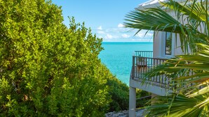 Une maison située sur la côte, dotée d’un balcon donnant sur la mer et entourée d’une végétation luxuriante.