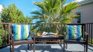 Une terrasse en bois avec deux fauteuils rembourrés et une table, agrémentée de coussins à rayures, d’une assiette de fruits et d’un verre de jus d’orange.