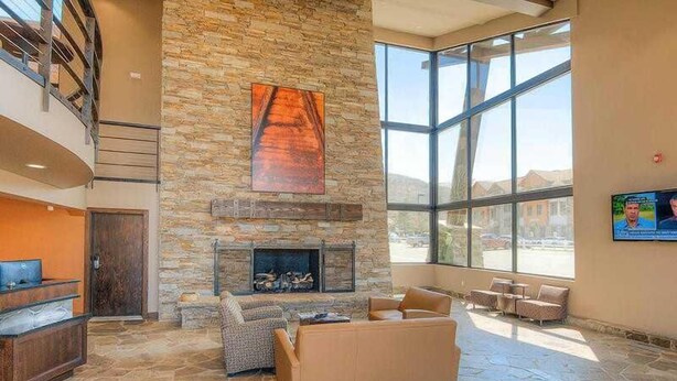A spacious lobby with a stone fireplace, comfortable seating, and large windows offering views of the outdoors. - Centrally Located Studio Condo, minutes from Main St and Skiing! (Park City)