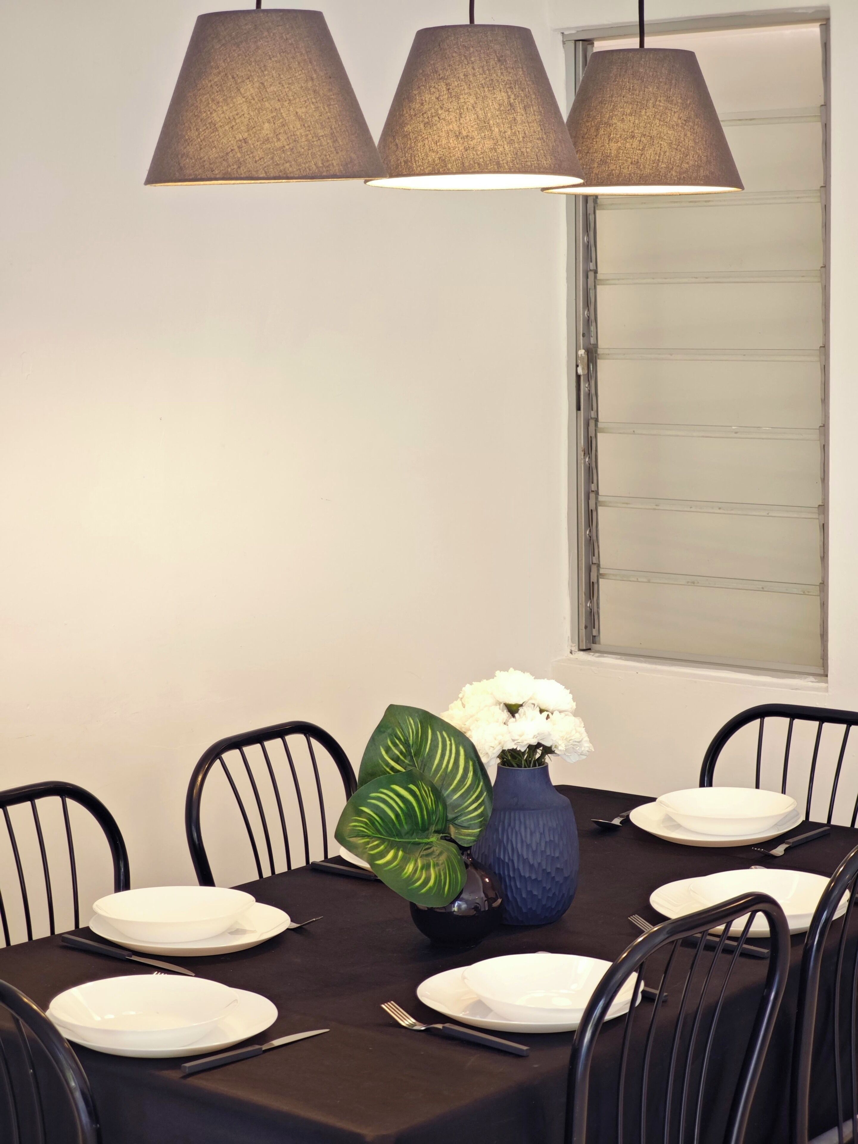 A dining table set for six with black chairs, a vase with white flowers, and a blue vase with green leaves.