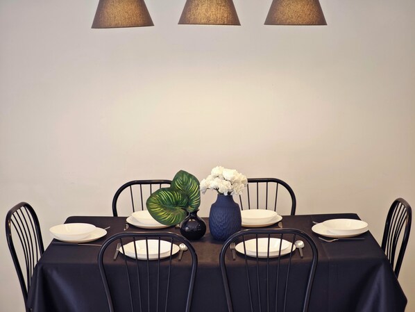 A dining table set with plates, cutlery, a vase with flowers, and a potted plant.