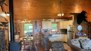 A cozy cabin interior with a stone fireplace, wooden dining table, and a living area with a sofa. - A beautiful log cabin home on Lake Huron, amazing lake views, hot tub, game room (Cheboygan)