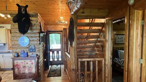 A log cabin interior with a wooden staircase, a bear head decoration, a clock, and a wooden dining table. - A beautiful log cabin home on Lake Huron, amazing lake views, hot tub, game room (Cheboygan)