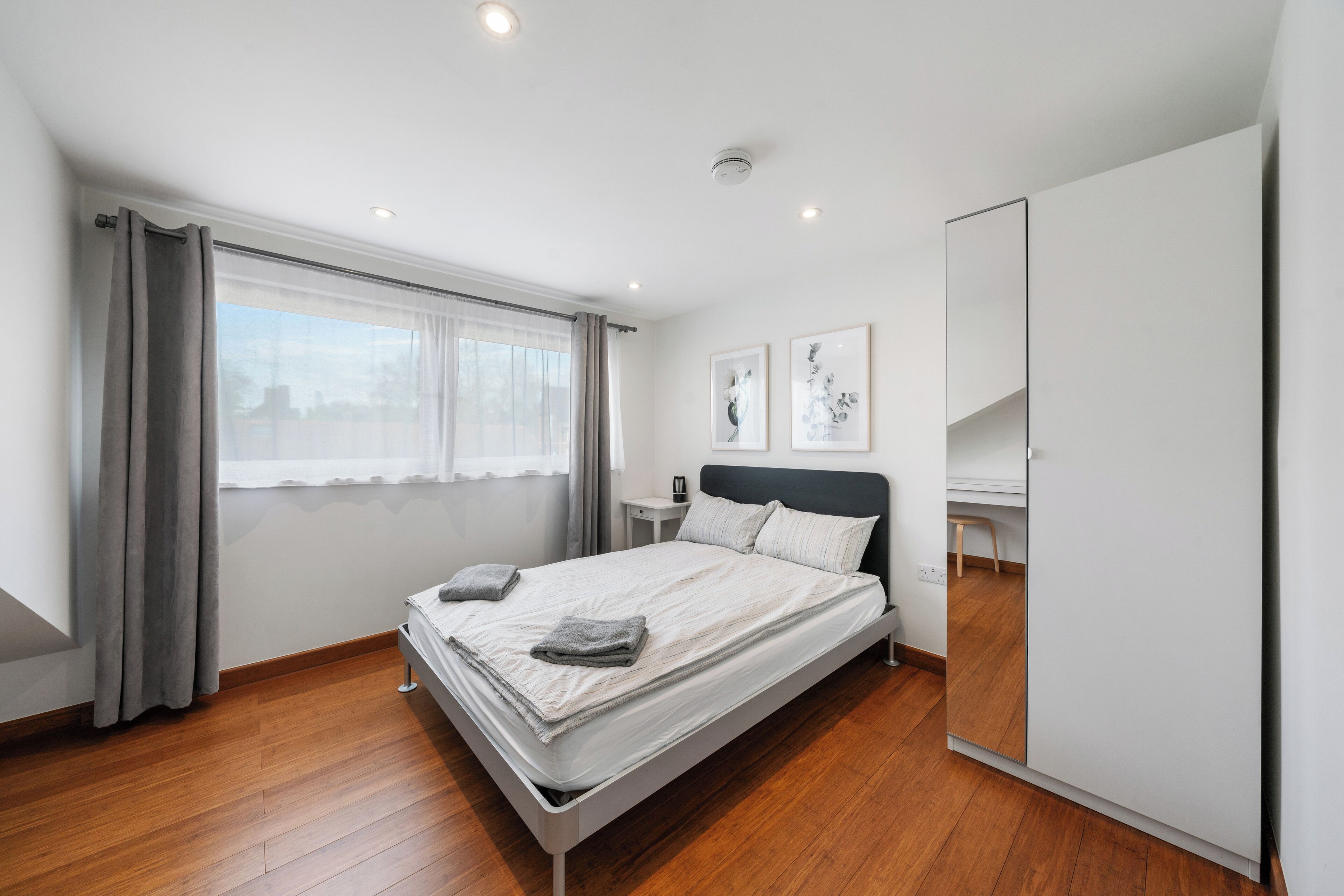 A modern bedroom with a bed, a nightstand, a mirror, and a window with curtains.