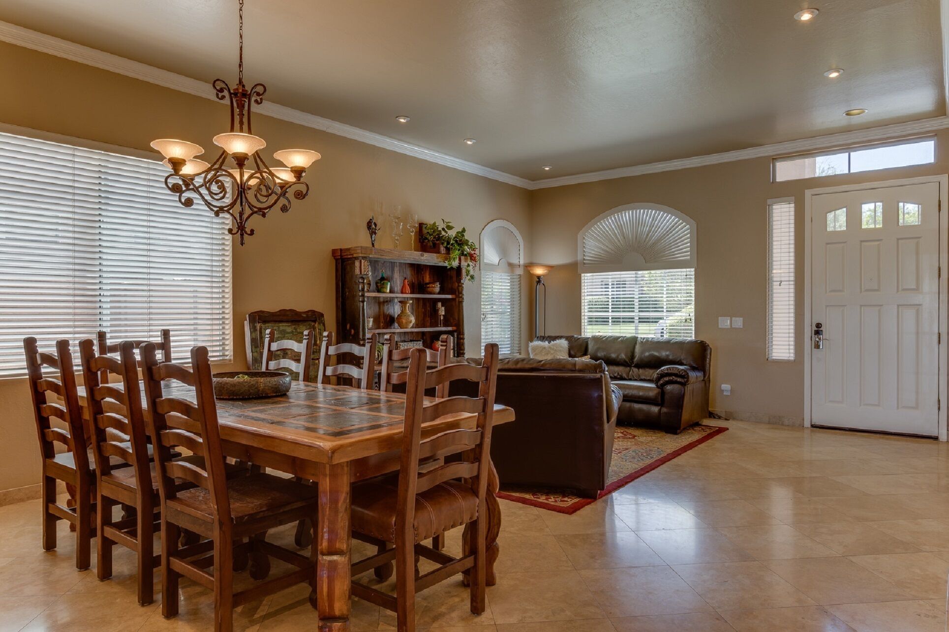 A spacious dining area with a wooden table and chairs, a chandelier, and a bookshelf with decorative items.