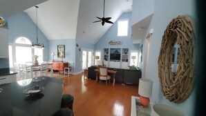 A spacious living area with a high ceiling, a dining area with a wooden table and chairs, and a kitchen with a large island.