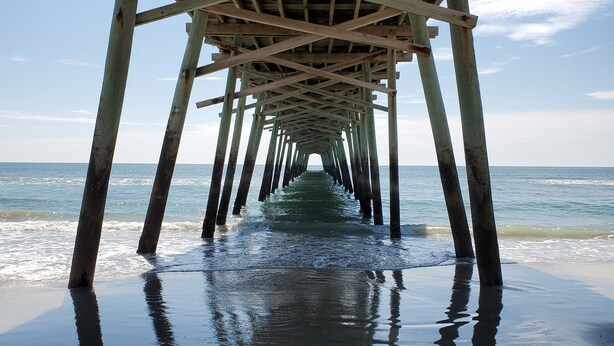 A wooden pier extending into the ocean with a clear sky above.