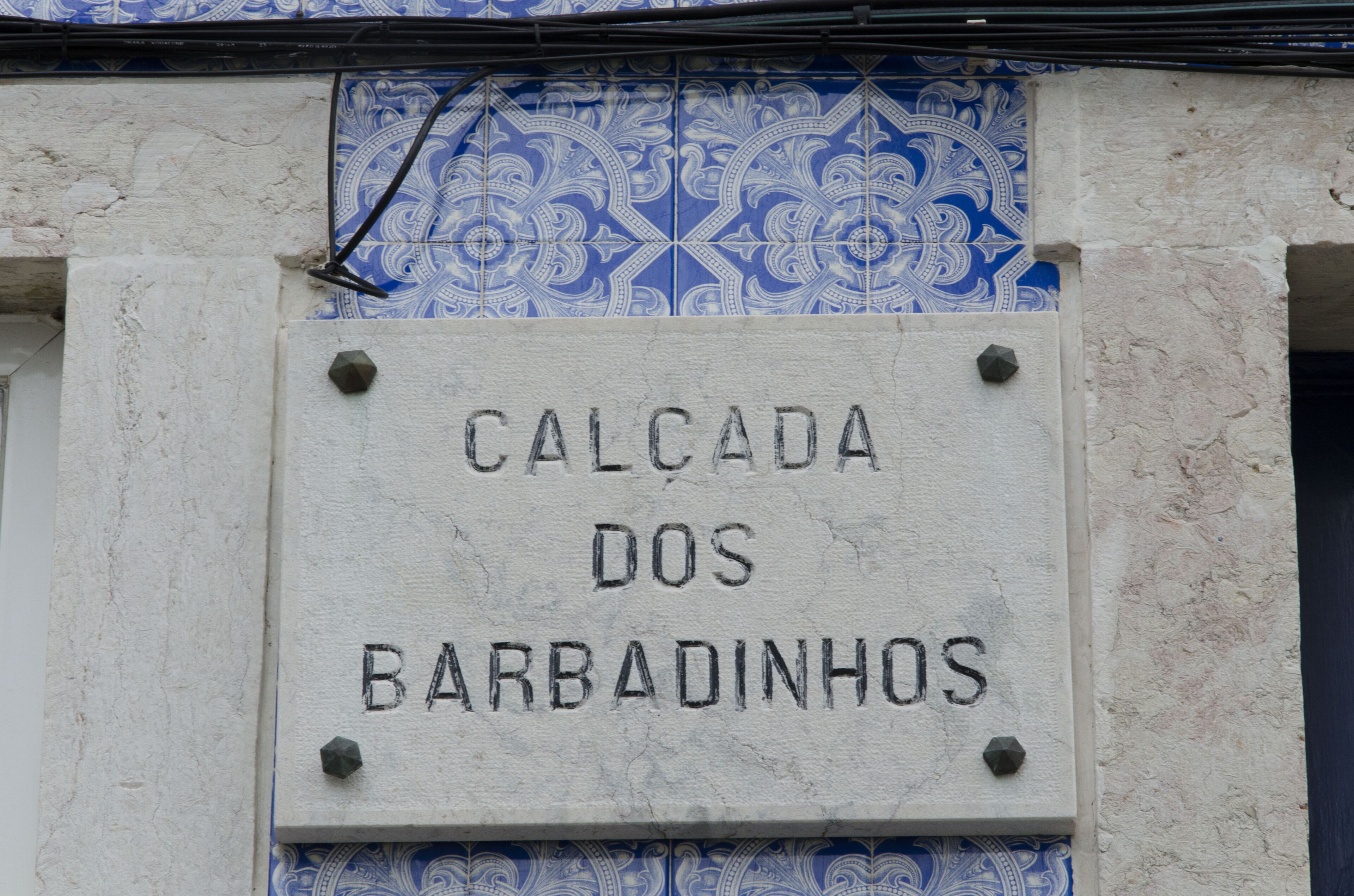 Señal con el texto 'CALCADA DOS BARBADINHOS' sobre fondo blanco, colocada en una pared con azulejos azules estampados.
