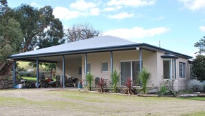 A single-story building with a covered porch, a garage, and a small garden with various plants. - Back Valley Farmstay Bed and Breakfast (Back Valley)