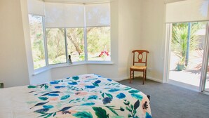 A bedroom with a large bed, a window with a view of greenery, and a chair. - Back Valley Farmstay Bed and Breakfast (Back Valley)