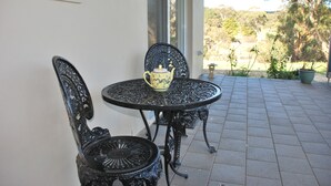 A patio with a round table and two ornate chairs, a decorative teapot on the table, and a view of a garden and trees through a glass door. - Back Valley Farmstay Bed and Breakfast (Back Valley)
