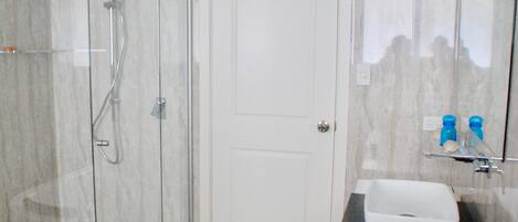 Un baño con ducha de vidrio, puerta blanca y lavamanos sobre encimera negra.