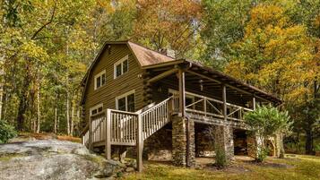 Une cabane en rondins avec des fondations en pierre, une terrasse en bois et un escalier en pierre menant à l’entrée.