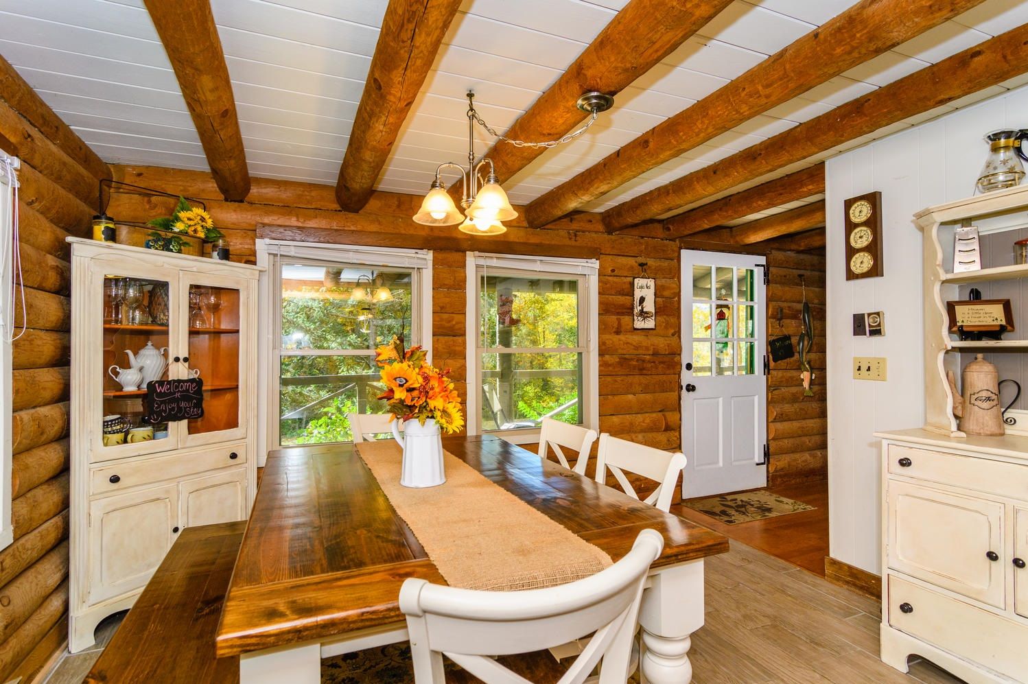 A wooden cabin interior with a dining table, chairs, a chandelier, and a coffee station.