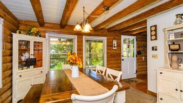 A wooden cabin interior with a dining table, chairs, a chandelier, and a coffee station.