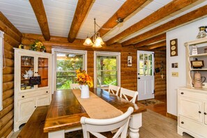 Een houten cabin met daarin een eettafel, stoelen, een kroonluchter en een koffiehoek.