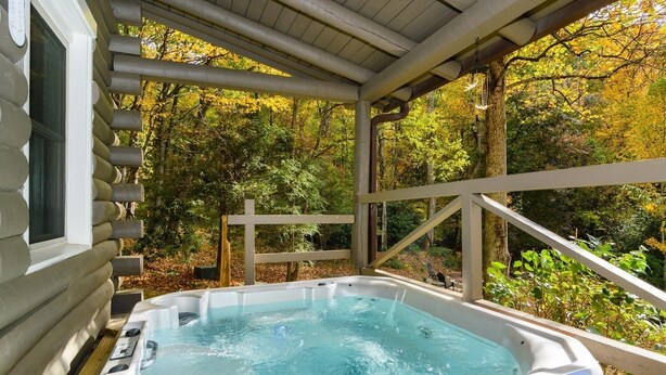 Een hottub in een overdekte buitenruimte met een houten terras en uitzicht op herfstbomen.