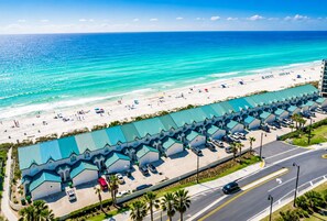 A beachfront hotel with a row of rooms, a parking lot, and a beach in the background.