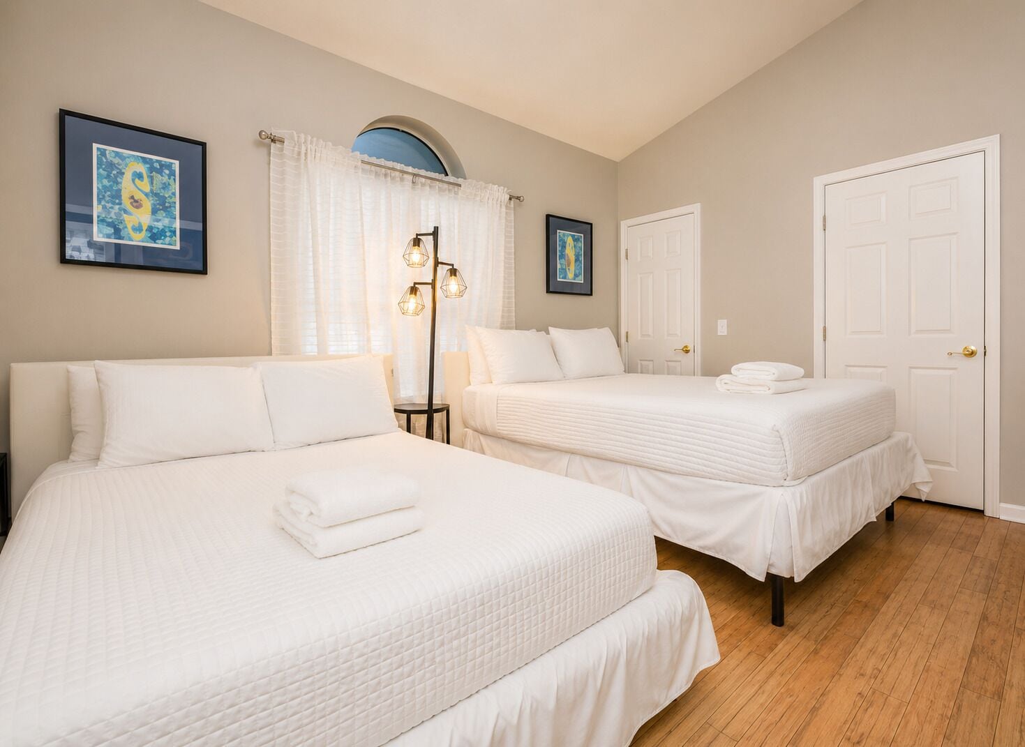 Quarto de hotel com duas camas, uma luminária de chão e uma porta.
