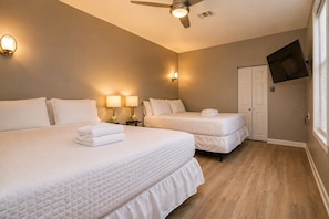 A hotel room with two beds, a ceiling fan, wall-mounted lamps, a TV, and a door.