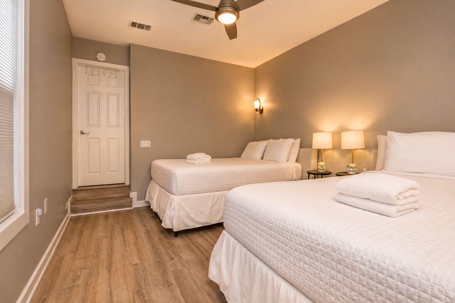 A hotel room with two beds, a ceiling fan, and bedside lamps.