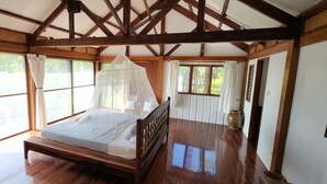 Une chambre avec un lit en bois, de grandes fenêtres et un plafond avec des poutres apparentes.