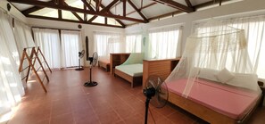 A room with a bed, a desk, a chair, a standing fan, and a window with curtains.