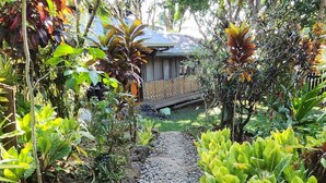 Un sentier de jardin bordé d’une clôture en bois, avec une végétation luxuriante et un bâtiment en arrière-plan.