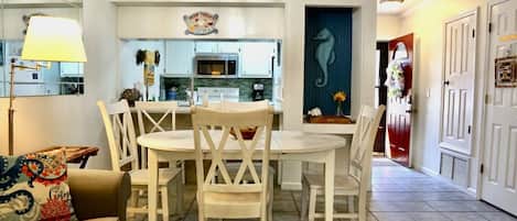 A dining area with a round table and white chairs, a kitchen with light blue cabinets, and a hallway with a seahorse wall art.