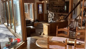 A spacious living area with wooden floors, a stone fireplace, and a dining table with chairs.