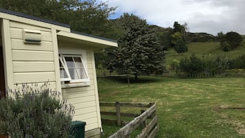 Situated in a rural setting, this charming cottage features a single-story design with a sheltered entrance and a wooden fence.