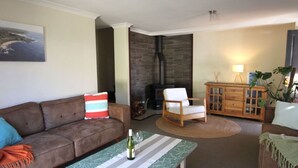 Un salon avec un canapé marron, une table à rayures, une chaise blanche, un meuble en bois et une cheminée.