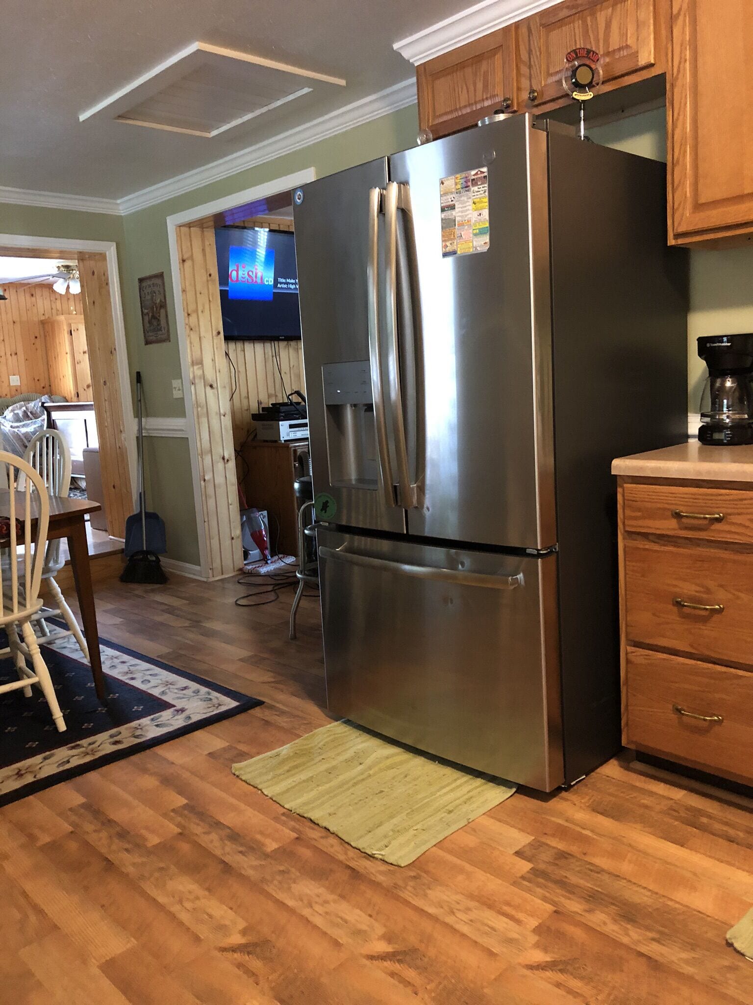 A kitchen with a stainless steel refrigerator, wooden cabinets, a coffee maker, and a television in the background.