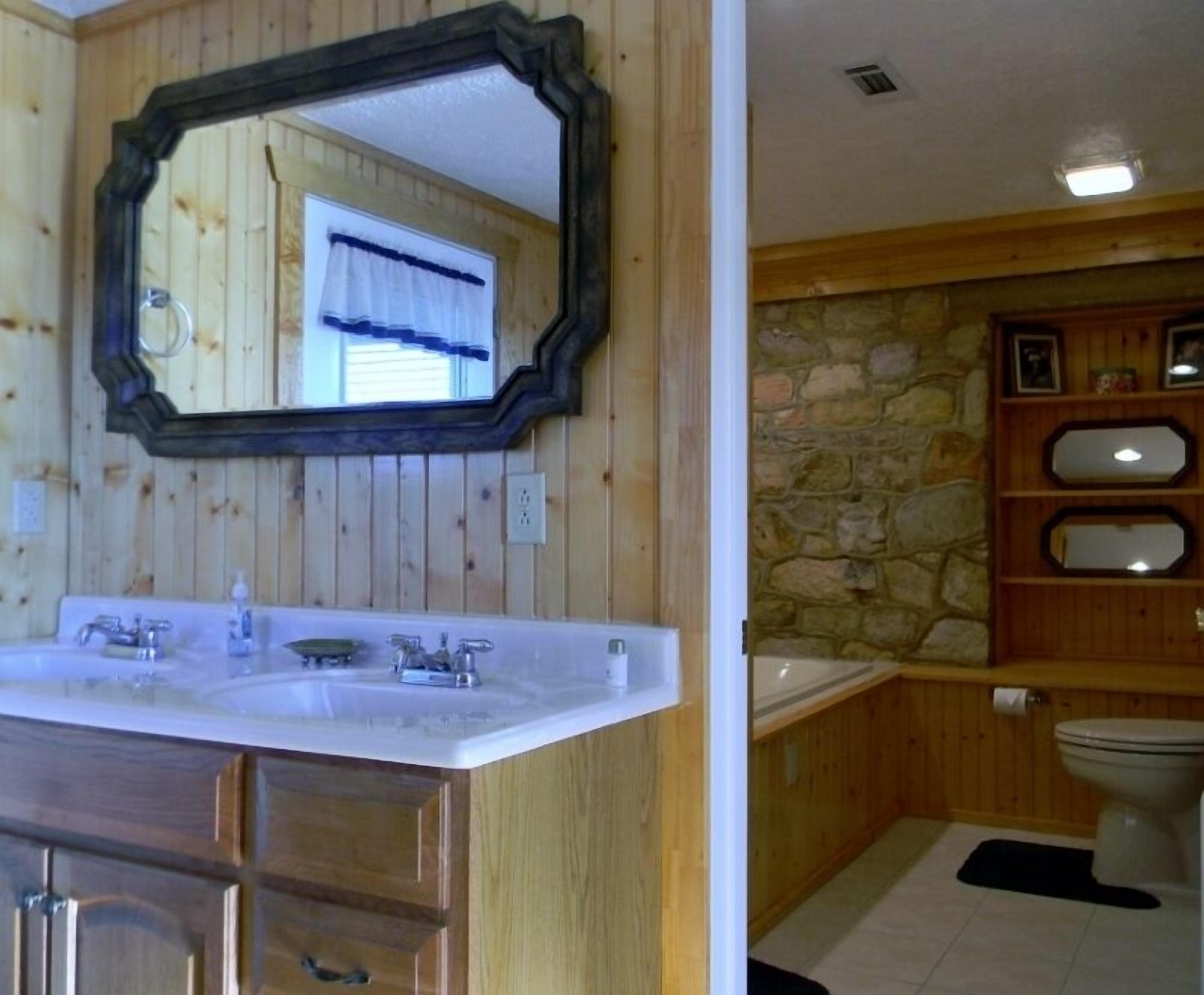 A bathroom with wooden paneling, a white sink, a mirror, a stone wall, and a toilet.