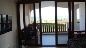 A room with a balcony, a bed, a TV, and a glass table. - Beach Front Apartment. (Diani Beach)