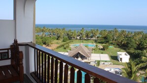 A balcony with a view of a resort, including a pool and palm trees. - Beach Front Apartment. (Diani Beach)