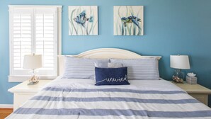 Een slaapkamer met een bed, twee nachtkastjes, een raam met zonwering en twee kunstwerken aan de muur.