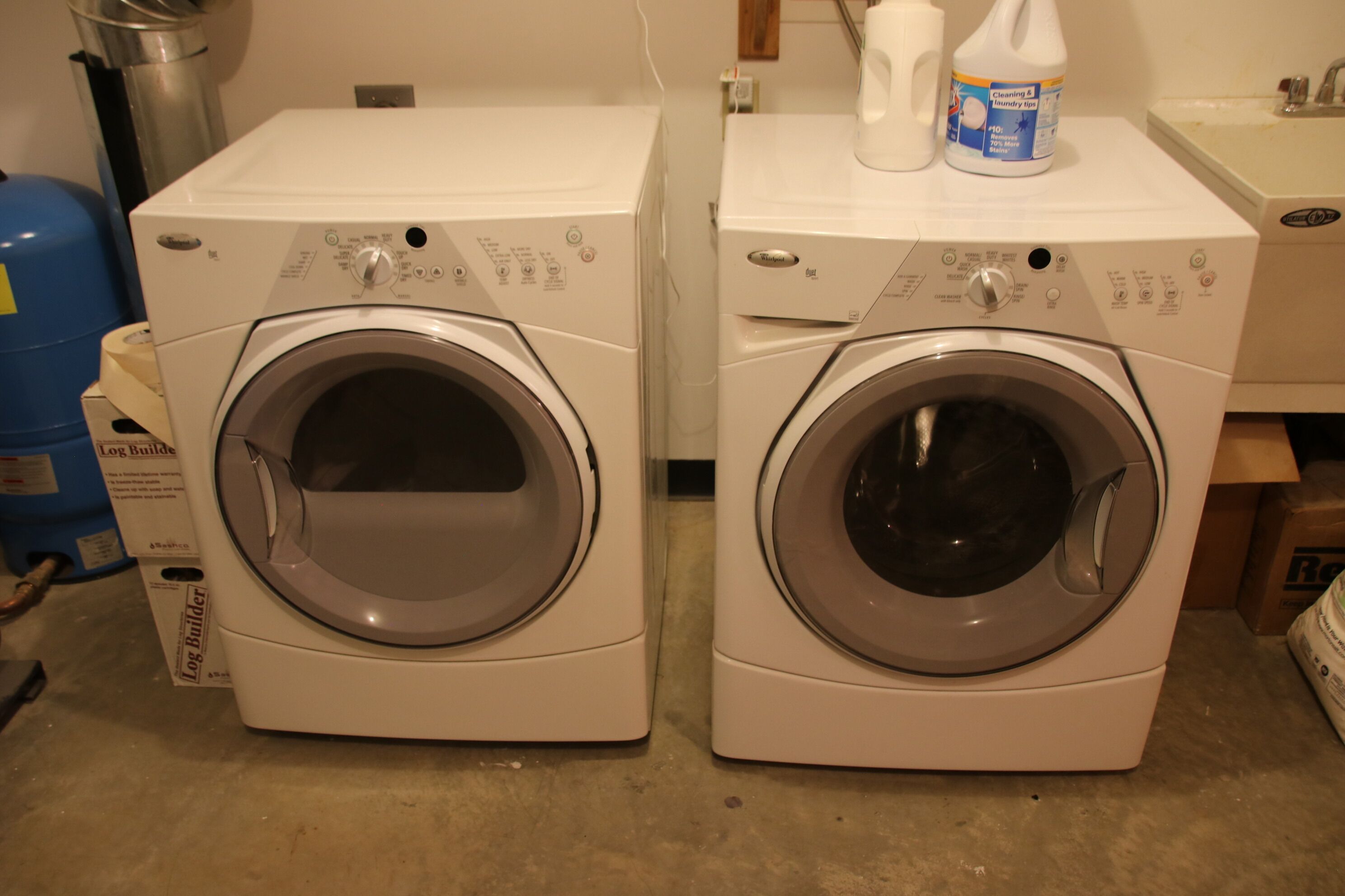 Two front-loading washing machines with control panels, a blue water heater, and a cleaning product on top.