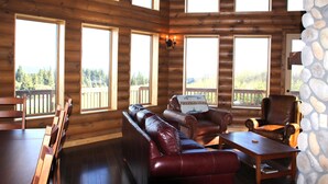 A log cabin interior with a wooden dining table, leather sofa, and stone accent wall.