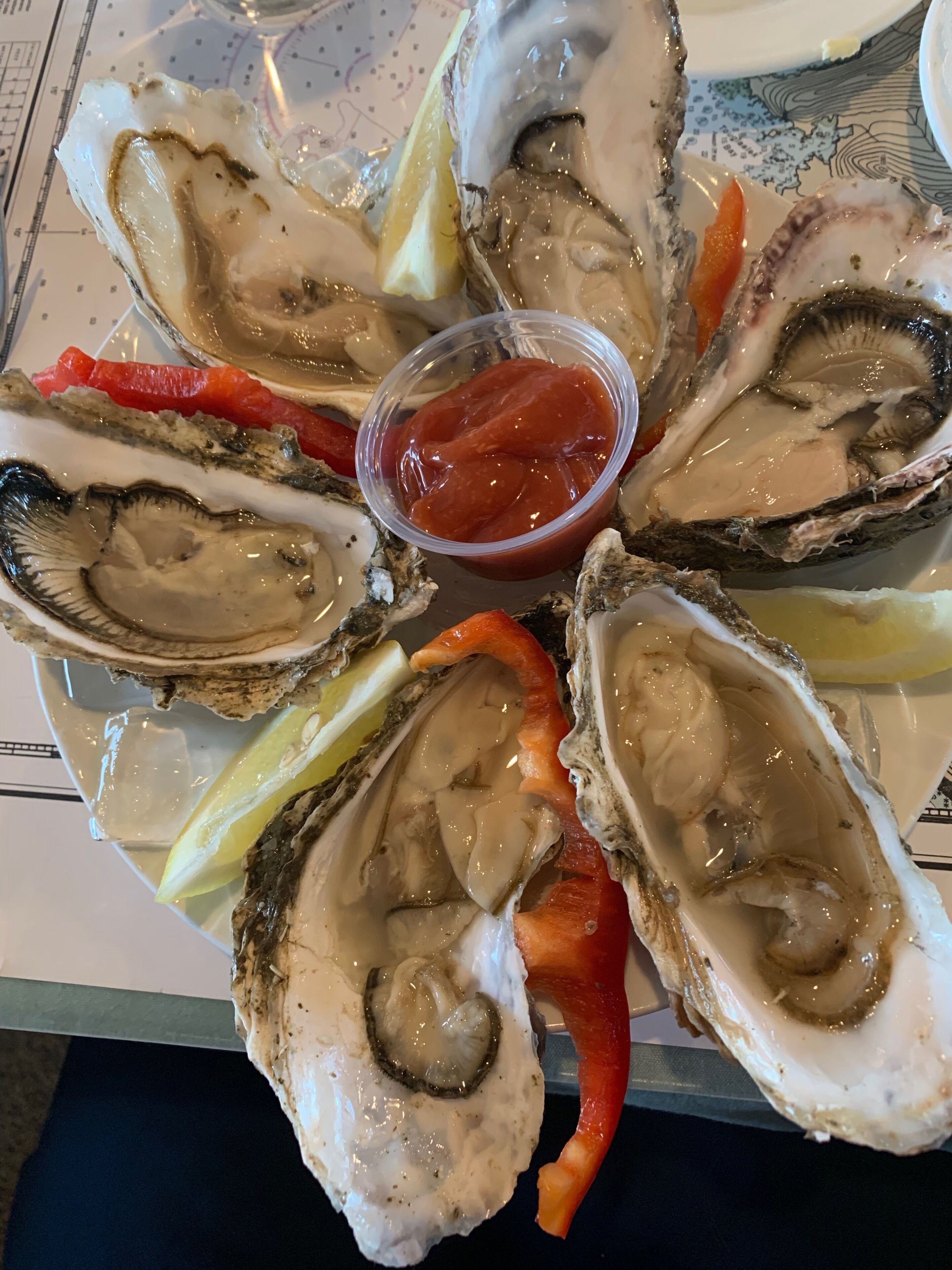 A plate of oysters with lemon wedges and a small container of sauce.