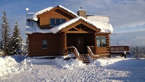 A wooden cabin with a snow-covered roof and steps leading to the entrance.