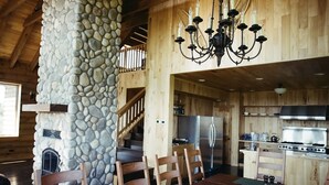 A rustic wooden interior with a stone fireplace, wooden dining table, and a kitchen area with modern appliances.